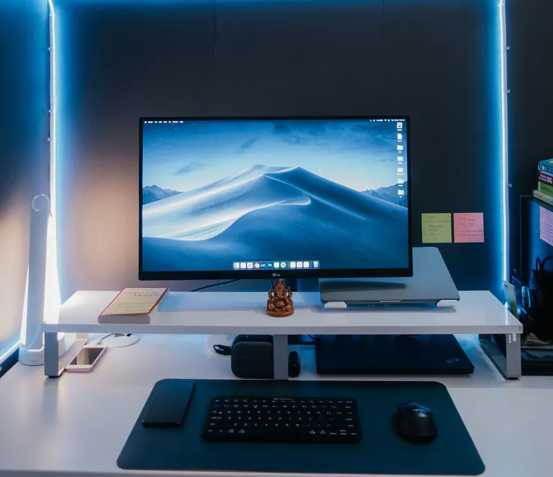 Modern desk setup with illuminated monitor, keyboard, mouse, and neat arrangement under soft neon lights