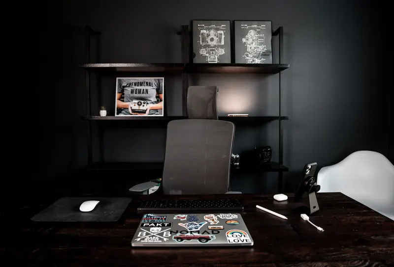 From above of creative design workspace with netbook with stickers on desk and shelf with images in frames