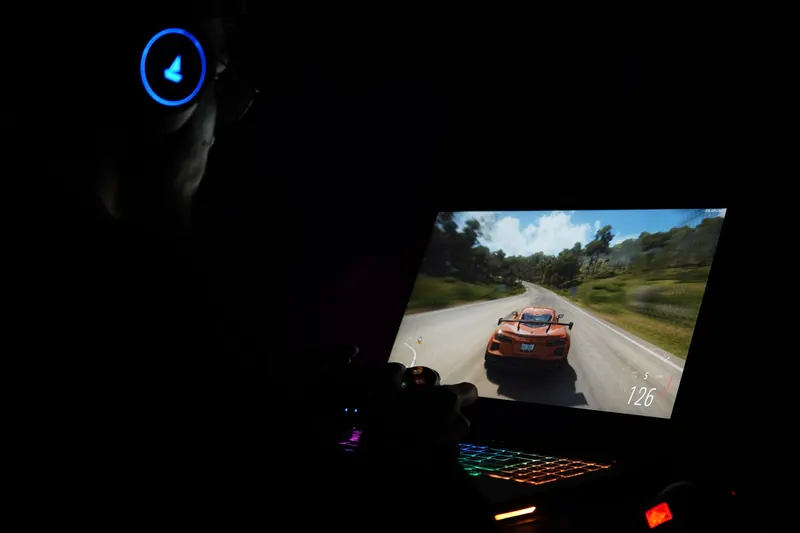 A gamer using a laptop and headphones to play a car racing game in a dark setting