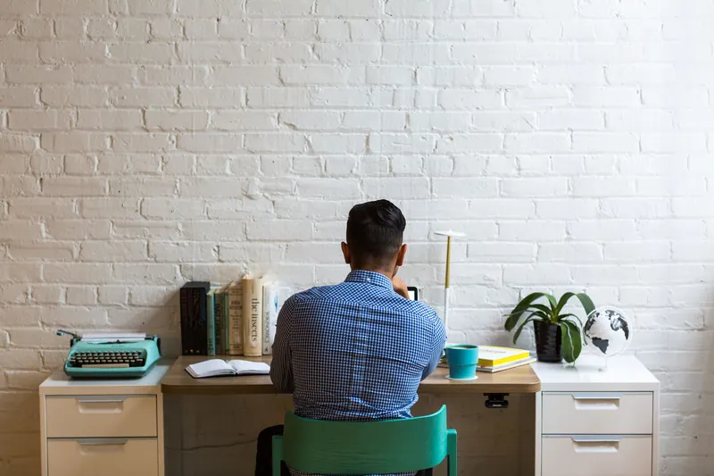 Back view of man at desk with typewriter and books, creating in a minimalist workspace