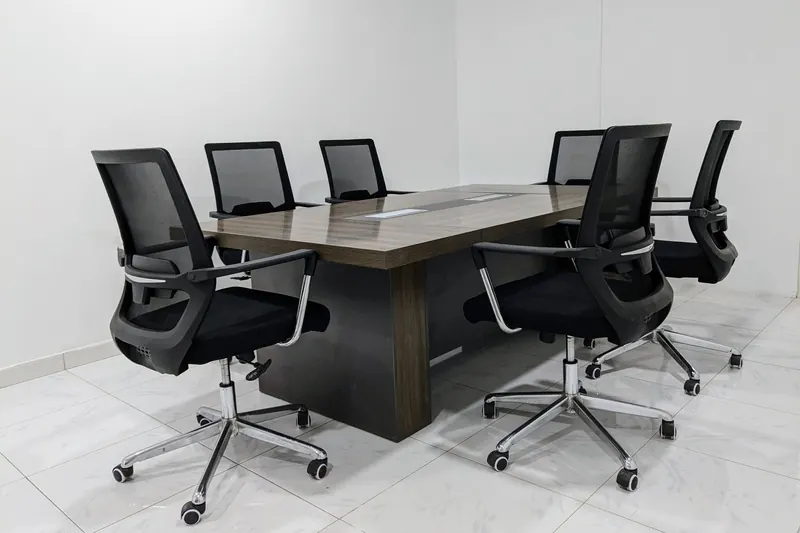 A neat and minimalistic conference room setup with black mesh chairs around a dark wooden table